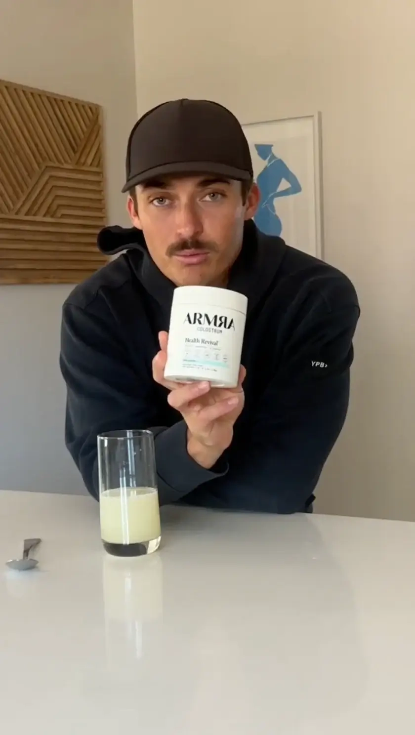 Man at a kitchen counter holding an ARMRA jar next to a glass