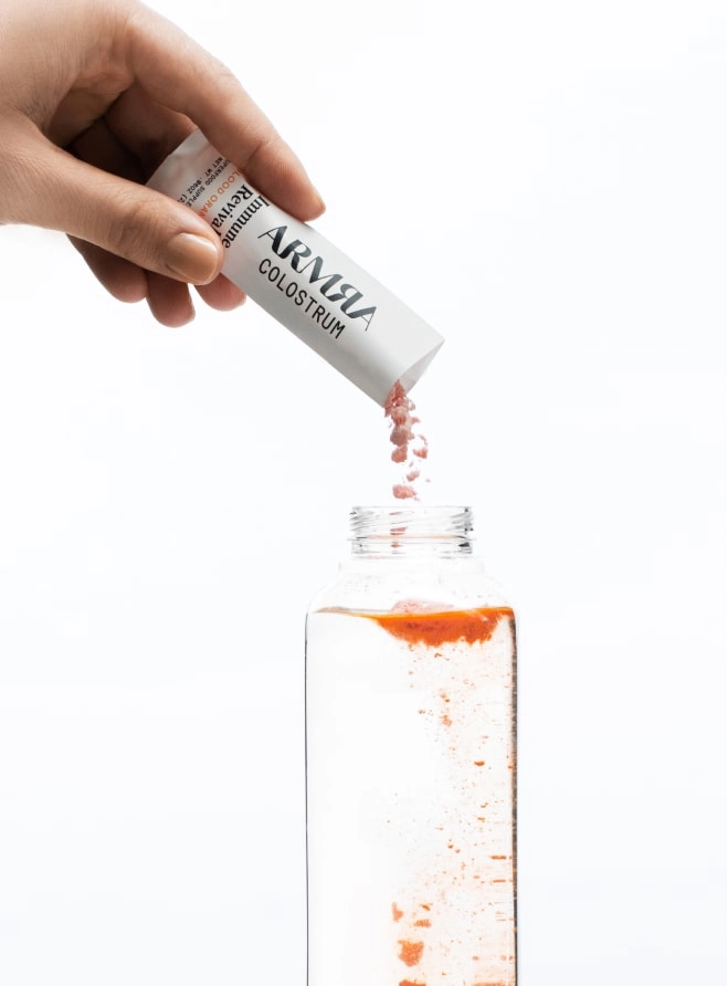 Hand pouring ARMRA colostrum sachet into water