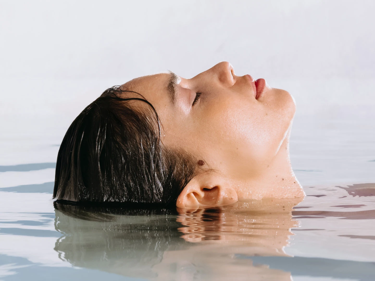 Person with closed eyes partially submerged in water against a light background