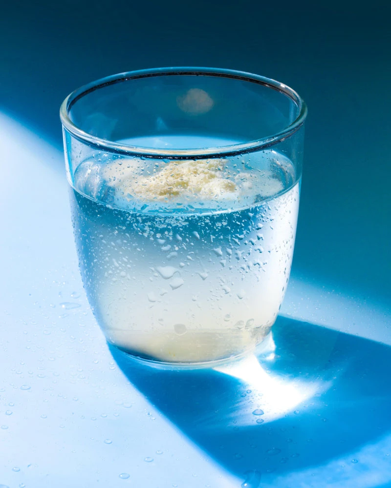Glass of sparkling water with powder dissolving, on a blue surface
